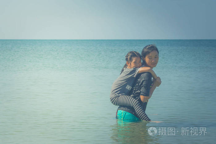 可爱和家庭概念 可爱的小女孩骑在女人背上, 他们站在海中, 感受幸福