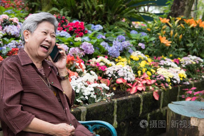 老妇人在花园里用手机说话。老年女性发言