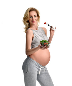 美丽的怀孕妇女举行有机沙拉和叉子与西红柿。孕产妇期望健康饮食