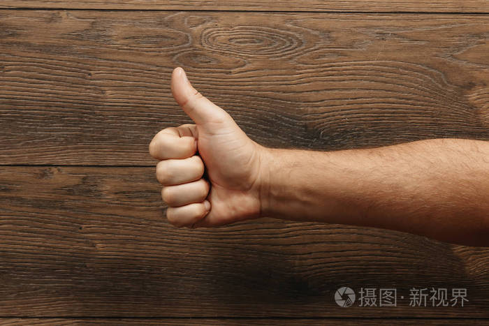 男人的手在木褐色的背景上显示大拇指
