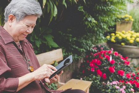 在花园里手持手机的老妇人。老年女性展览会