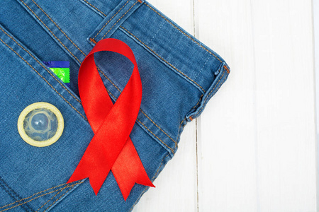 蓝色牛仔裤背景上的红丝带和避孕套.认识和预防艾滋病,艾滋的概念.