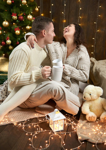 夜晚室内快乐的情侣喝茶, 在圣诞装饰, 坐在地板上, 在黑暗的木制室内