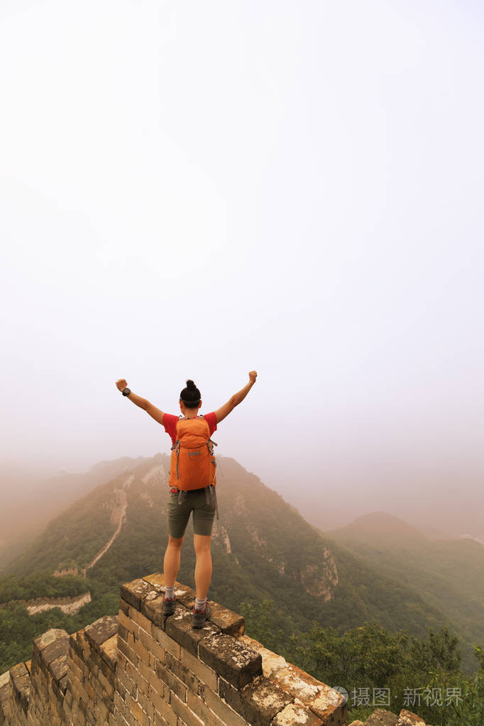 成功的女徒步者站在山顶的长城上张开双臂
