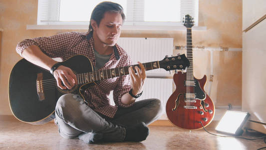年轻有吸引力的音乐家演奏吉他坐在地板在厨房