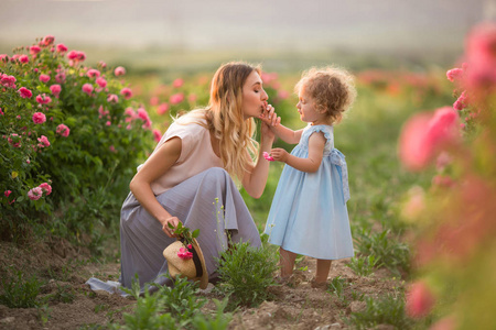 美丽的夫妇孩子女孩与母亲走在春天花园与粉红色开花玫瑰花, 日落时间