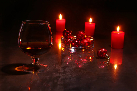 圣诞节装饰。一杯干邑或威士忌, 红色的蜡烛和彩色的木制背景球