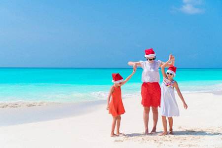 在一个热带海滩上庆祝圣诞节的妈妈和孩子们的幸福美丽的家庭在红色圣诞老人帽子