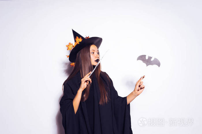 万圣节女巫穿着的年轻性感哥特式女孩拿着一根魔杖