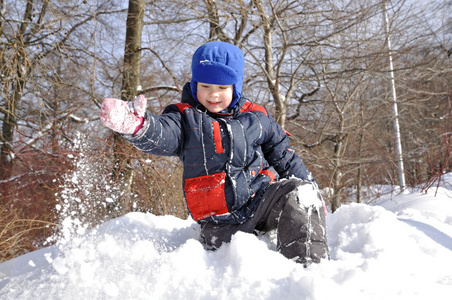 一个小男孩在冬天的雪堆上扔雪。