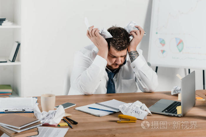 疲倦的超重的生意人坐在工作场所与皱巴巴的纸