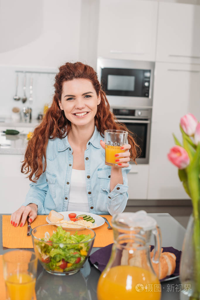 微笑的女孩坐在餐桌上吃饭, 拿着一杯橙汁