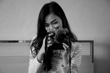年轻漂亮的亚洲女人坐在床上拍照数码单反光相机黑白图片