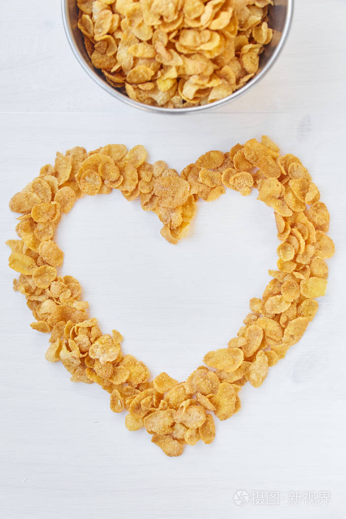 在一个彩色的白色木制背景的金属碗中的玉米片.