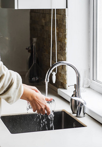 妇女手洗盘子或倾吐的玻璃与奔跑新鲜的饮料水在厨房水龙头