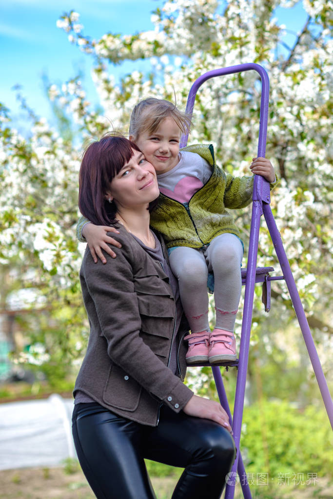 女儿亲切地拥抱她的母亲背景一朵盛开的春天树
