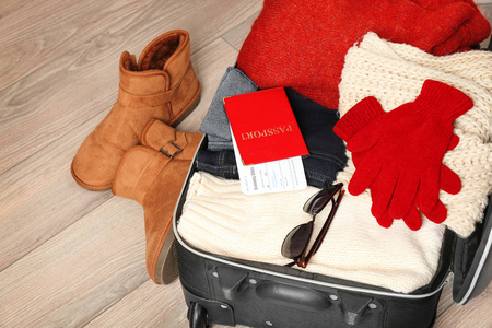 在木地板上用暖和的衣服和文件打开手提箱。寒假概念