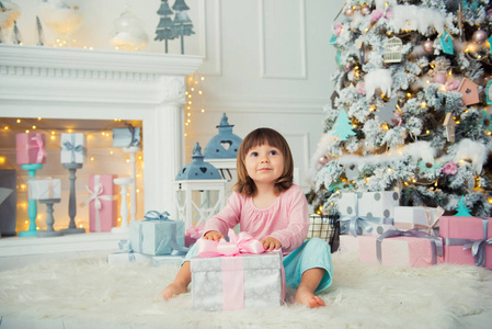 积极开朗的女婴坐在圣诞节礼物圣诞树附近。新年快乐