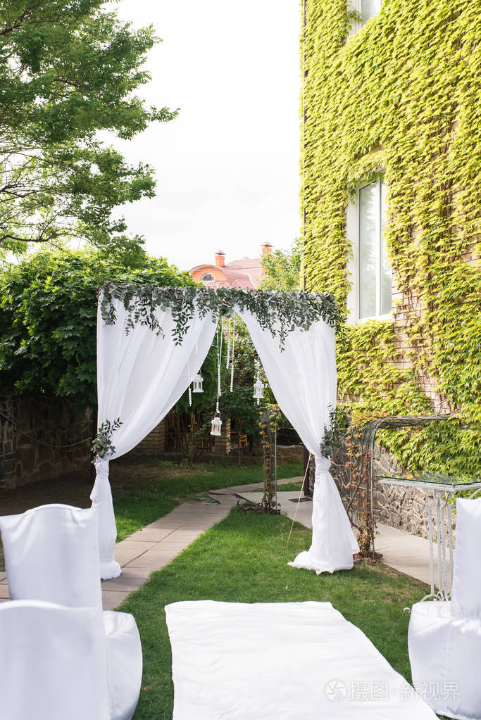美丽的方形婚礼拱门, 装饰着白色的材料和绿叶, 站在花园为新婚夫妇和他们的客人