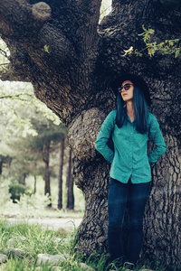 休闲风格的年轻女子与蓝色的头发站在橡树旁