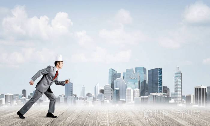 年轻英俊的生意人佩带白色纸冠奔跑在都市的匆忙与城市背景