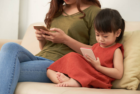 小女孩看动画片在智能手机屏幕与母亲在沙发上