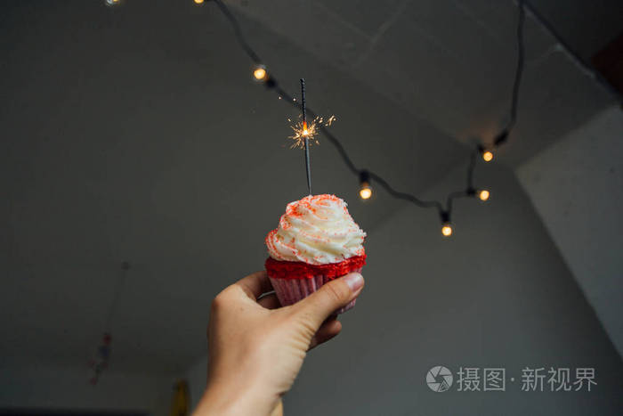 妇女手捧着粉红色的蛋糕与霜和奶油顶对房间墙与花环