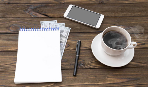 一杯咖啡, 智能手机, 美元, 记事本和木桌上的钢笔