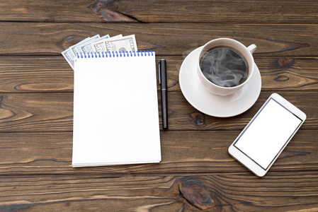 一杯咖啡, 智能手机, 美元, 记事本和木桌上的钢笔。财务规划概念