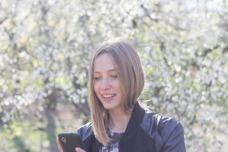 年轻女性在春天公园里摆着智能手机, 背景是白色的花朵