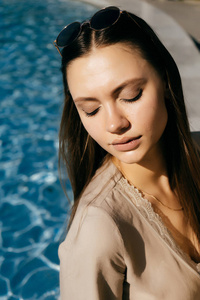 可爱的女孩在游泳池边休息。戴眼镜的女孩低头