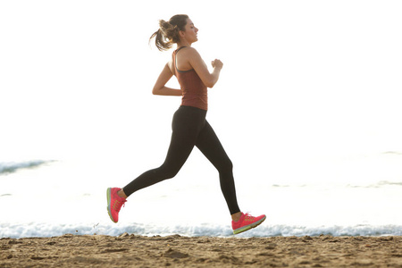 美丽的女性慢跑在海滩上的全长肖像锻炼例行