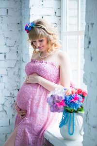 笑着，看着肚子里，手捧鲜花的孕妇。粉红色的连衣裙