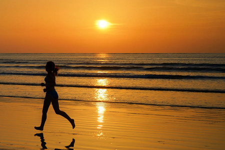 女人慢跑者在反思 健身与体育概念的日落海滩上运行的剪影