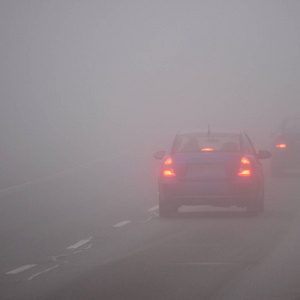 在雾中的汽车。恶劣的冬季天气和危险的汽车交通的道路上。轻型车辆在雾中