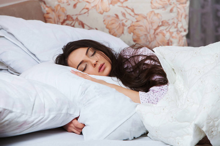 女孩在家睡在一张白色的床上。睡在睡衣上的年轻女子在家里的白色亚麻布, 顶部视图