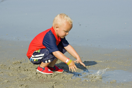 男孩在海滩上的沙子中扮演