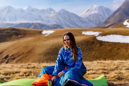 可爱的年轻女孩穿着蓝色夹克坐在高加索山脊的背景, 享受自然