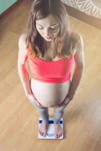 怀孕的妇女站在磅秤上的房间。孕期体重减轻与控制的概念