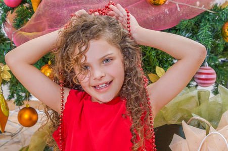 幸福的女孩穿着红色的礼服, 手持圣诞装饰在她的头上, 与圣诞树的背后, 圣诞节的概念
