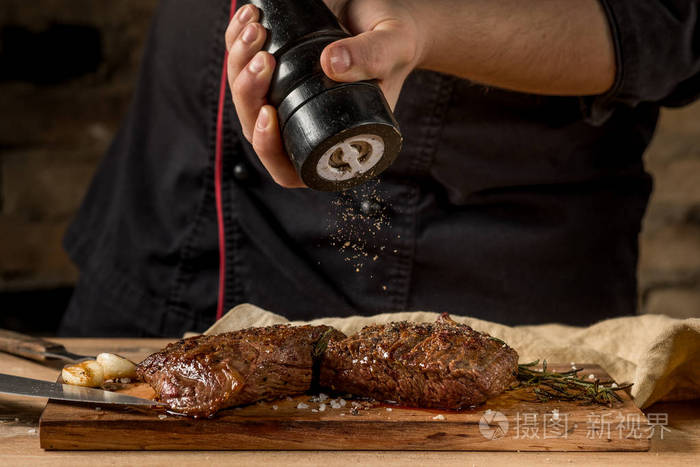 厨师加胡椒粉, 配有磨黑背景的牛排.食品食谱照片