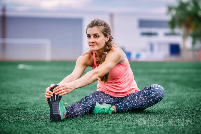 一个穿着紧身衣和背心的漂亮肌肉女孩在体育场里做热身运动.