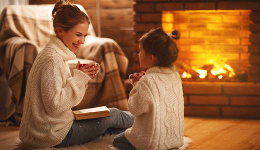 家庭母亲和孩子读书书在冬天晚上由 firepl