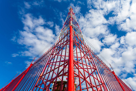 通信塔与小组天线和无线电天线和卫星盘子为移动通信 2g, 3g, 4g, 5g 与红色篱芭在塔附近反对蓝色与云彩