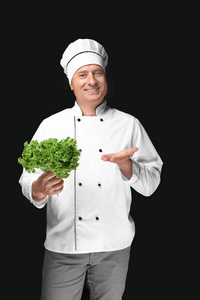 男性厨师在黑色背景下保持绿色沙拉