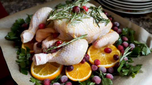 全生鸡与新鲜欧芹小红莓和橙片的特写视图烤盘锡准备烘烤