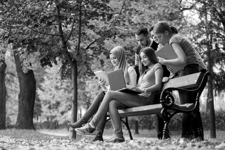 一群年轻人在公园长椅上使用笔记本电脑和片剂, 玩得开心, 聊天, 闲逛