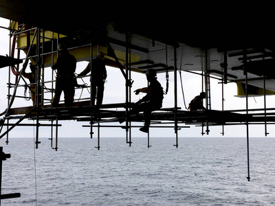 石油和天然气工业。海上防坠落装置海上作业人员剪影在海中油气平台下工作