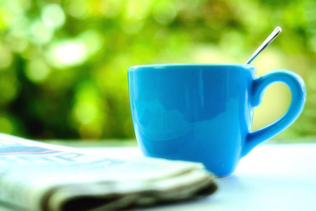 蓝色咖啡杯与模糊的报纸和天然绿色背景的选择性和软焦点