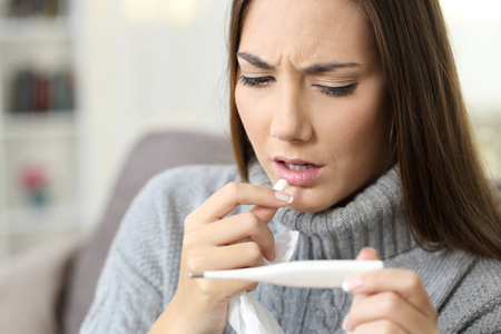 发烧的女人看着温度计吃药丸